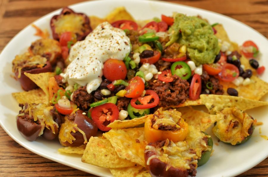 A plate of nachos topped with meat, tomatoes, beans, guacamole and sour cream. 